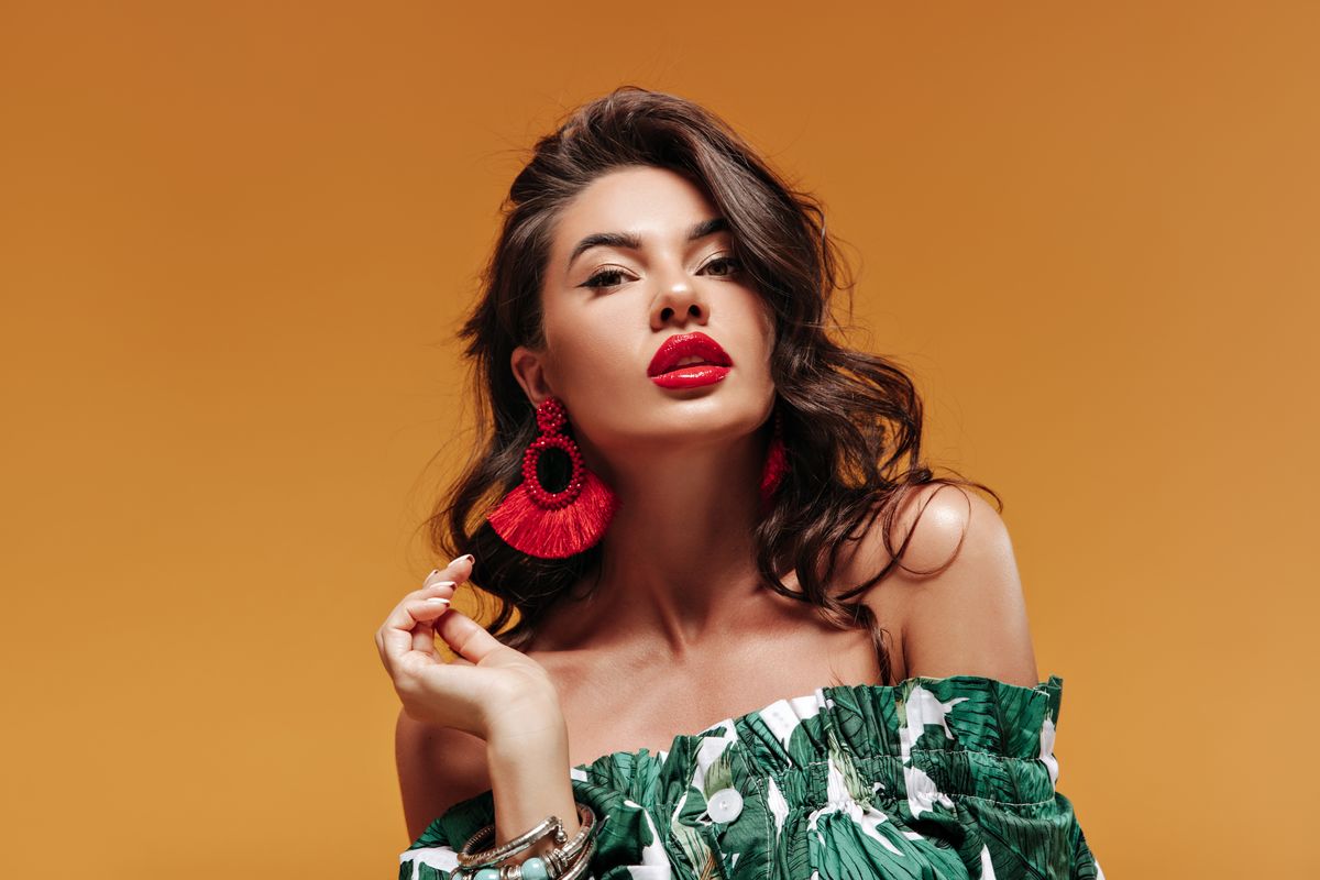 Trendy attractive woman with wavy hairstyle with modern cool earrings and big red lips in green sun